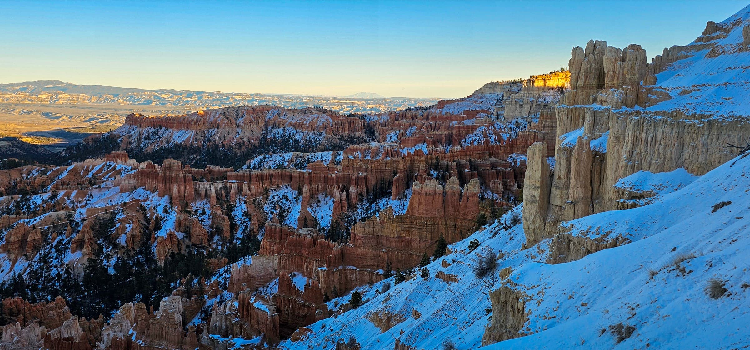 Snow-dusted red-rock hoodoos of Bryce Canyon lit by dawn alpenglow, cold shadow in the amphitheater below.