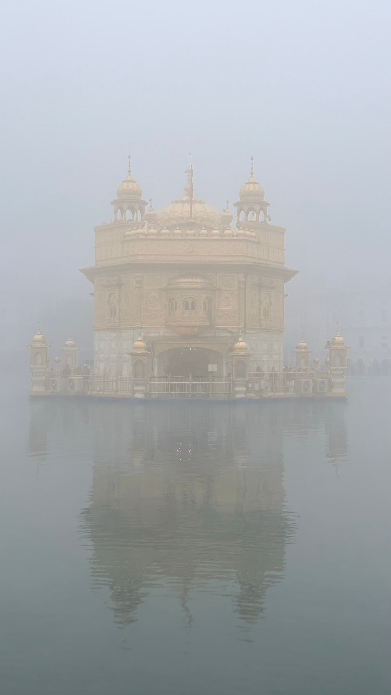 The Golden Temple of Amritsar emerging from dense fog, reflected in still water.