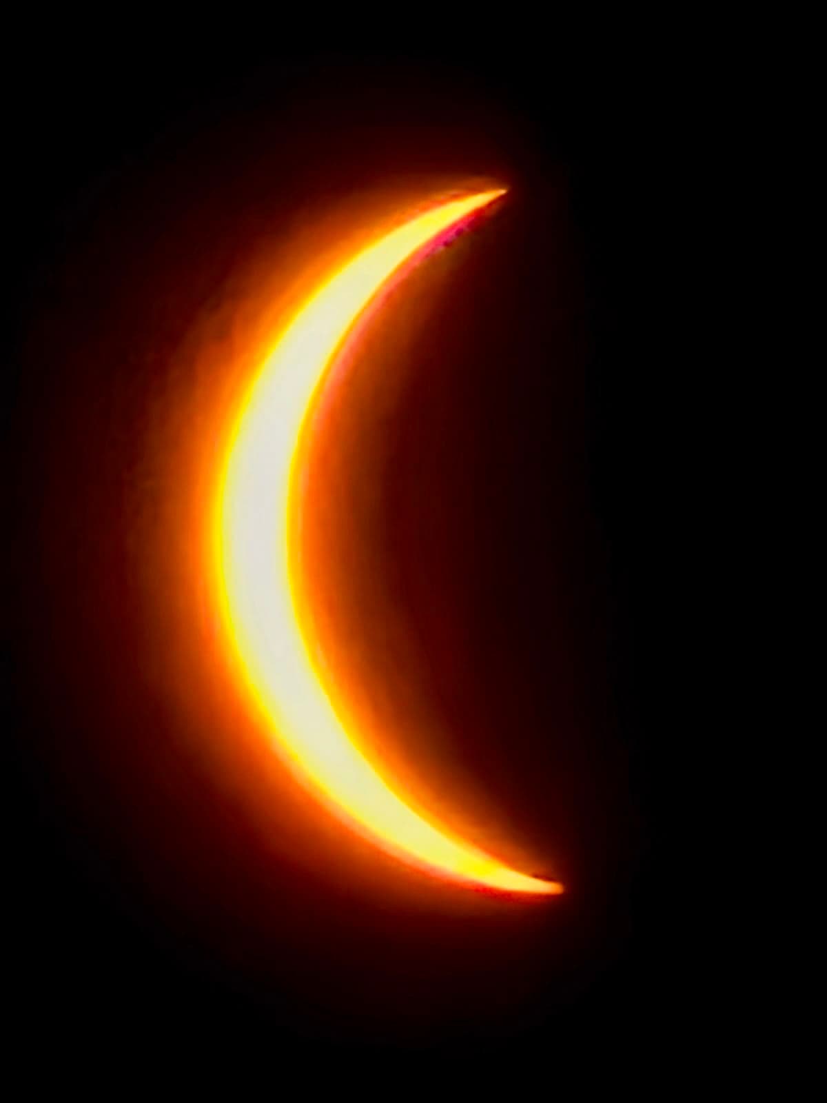 A thin orange crescent of sun against a black sky during a solar eclipse.